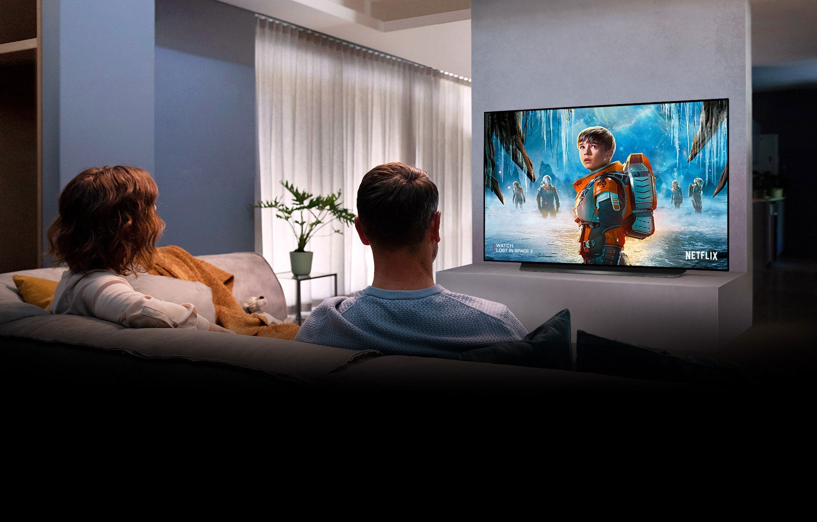 Couple sitting on a sofa in the living room watching a romantic movie on TV