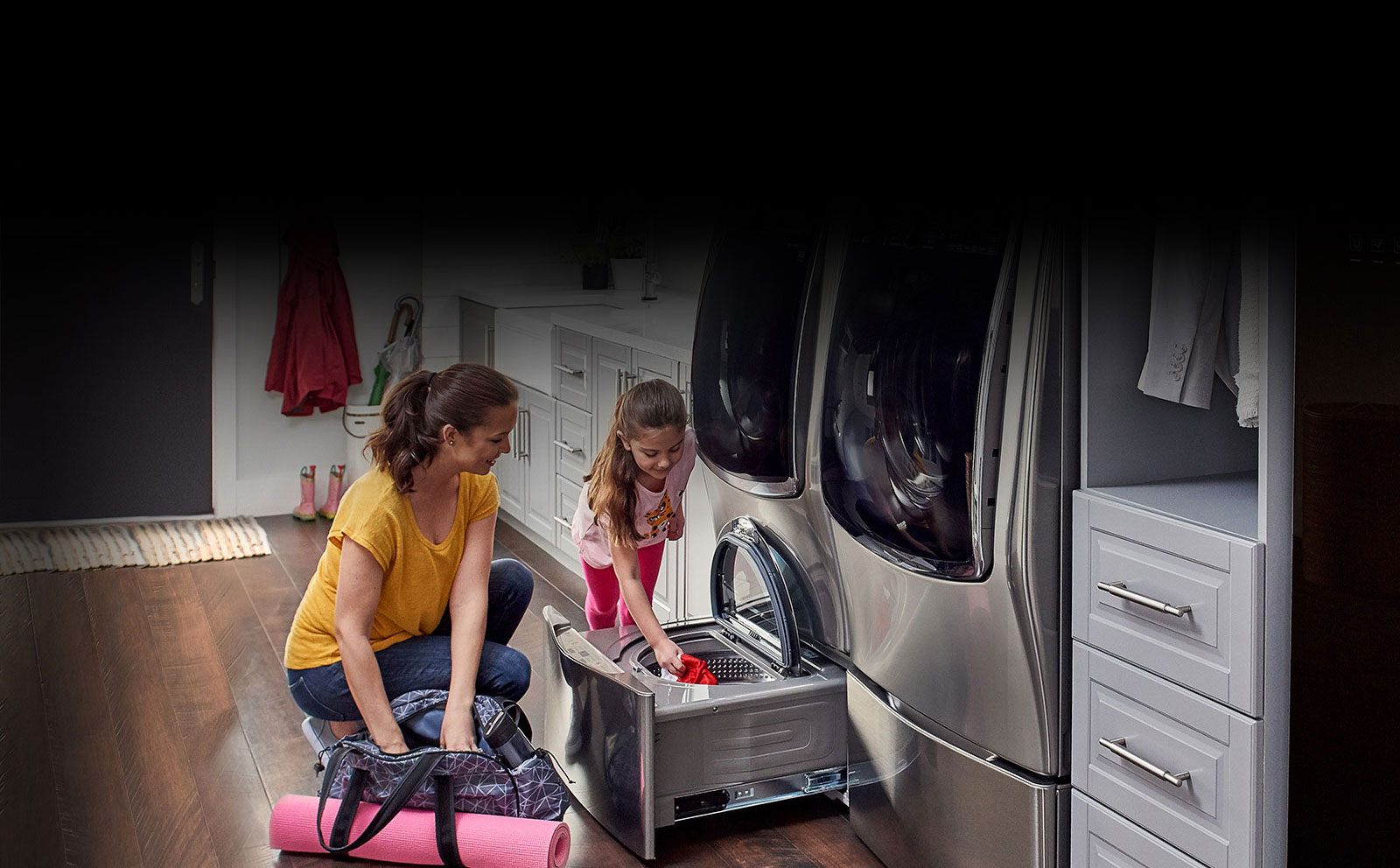 Woman and child placing clothes inside the pedestal washer