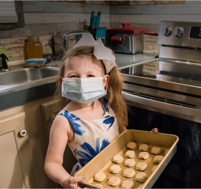 A girl wearing a mask and holding a tray with cookies