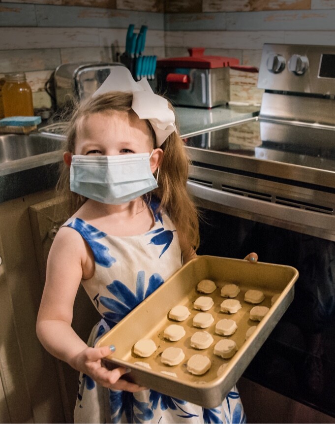 A girl wearing a mask and holding a tray with cookies