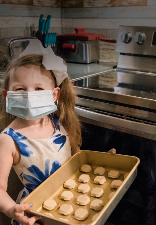 A girl wearing a mask and holding a tray with cookies