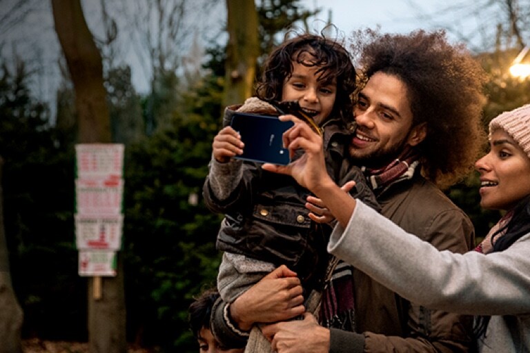 A man holding a child and a woman taking selfies together.