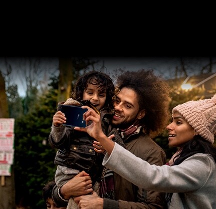 A man holding a child and a woman taking selfies together.