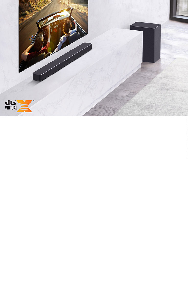 TV is on the wall, LG Soundbar is below on a white marble shelf with a sub-woofer to the right. TV shows a couple in a car.