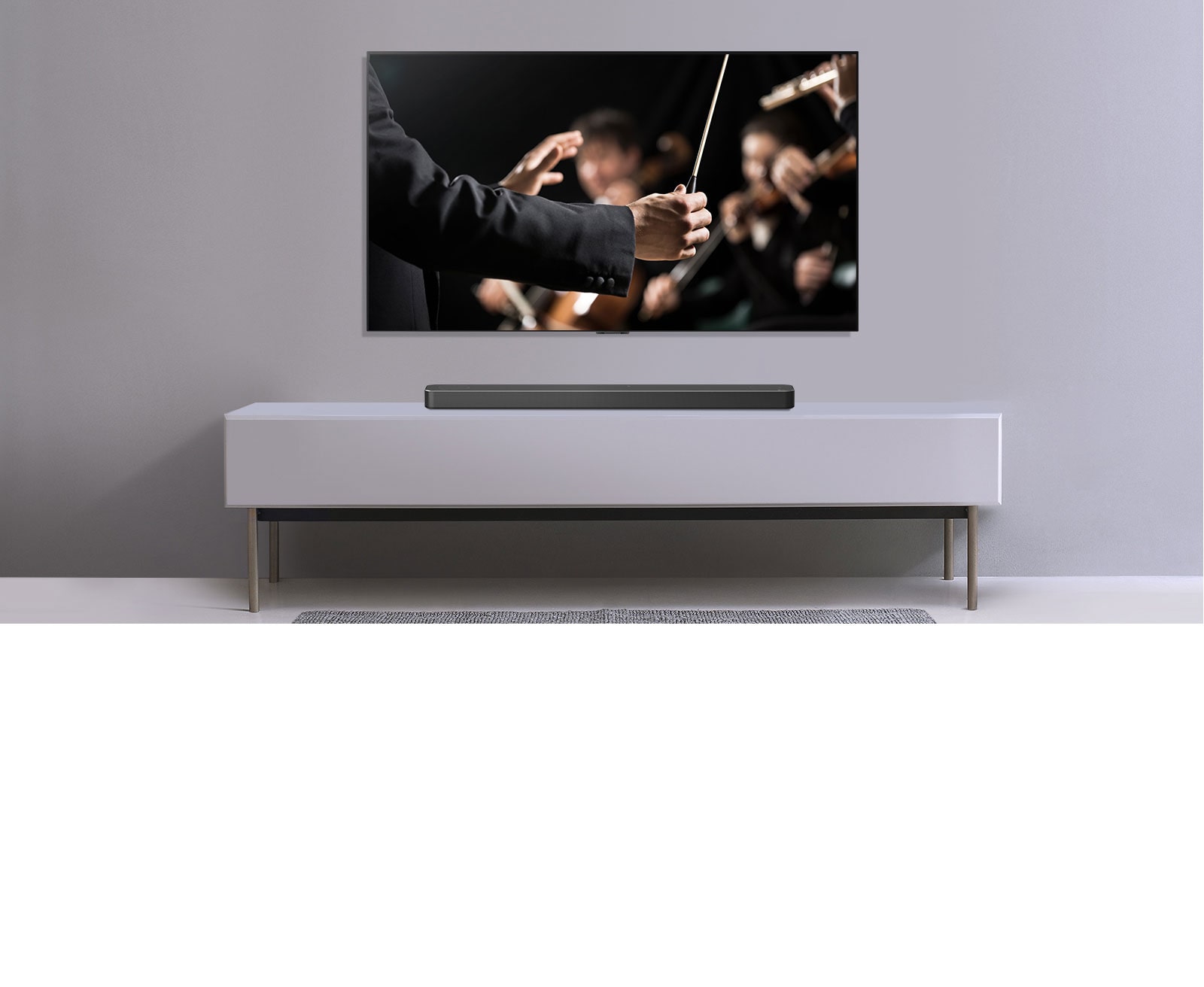 A TV is shown on a gray wall and LG Soundbar below it on a gray shelf. TV shows a conductor conducting an orchestra.