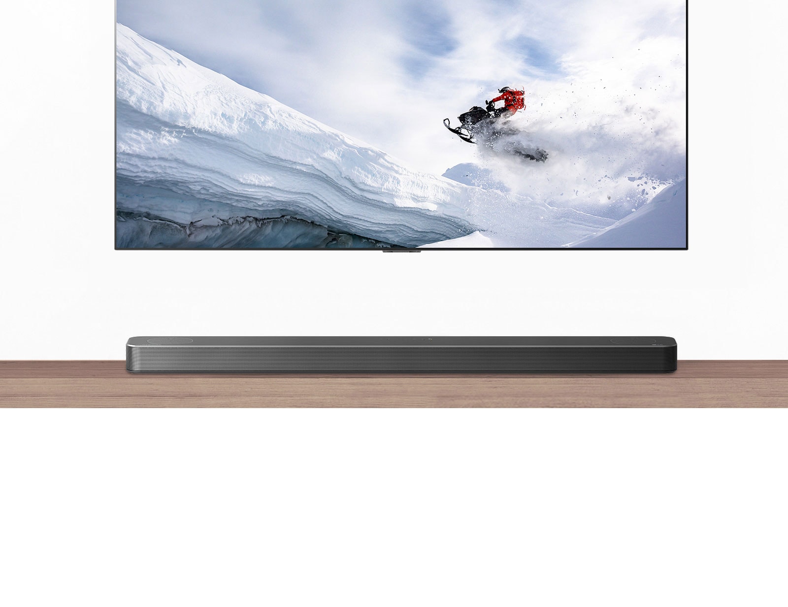 TV and Soundbar are seen from the front. TV shows man riding snowmobile in the snowy mountains. HDMI 2.1 logo is below TV.