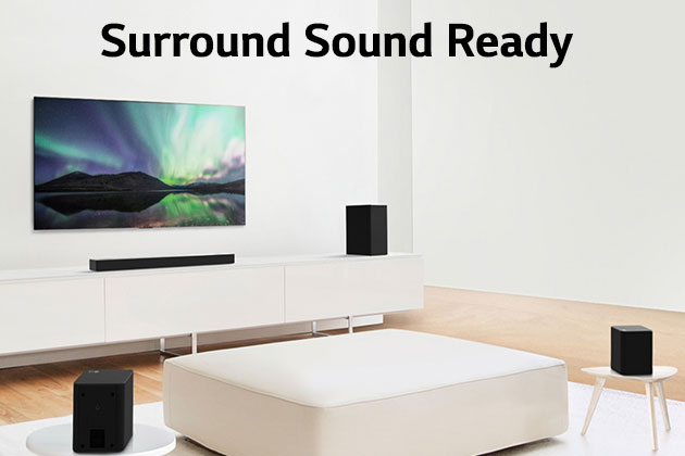 TV and sound bar in white living room with white sofa in the center. Speakers sit on both ends of the sofa.