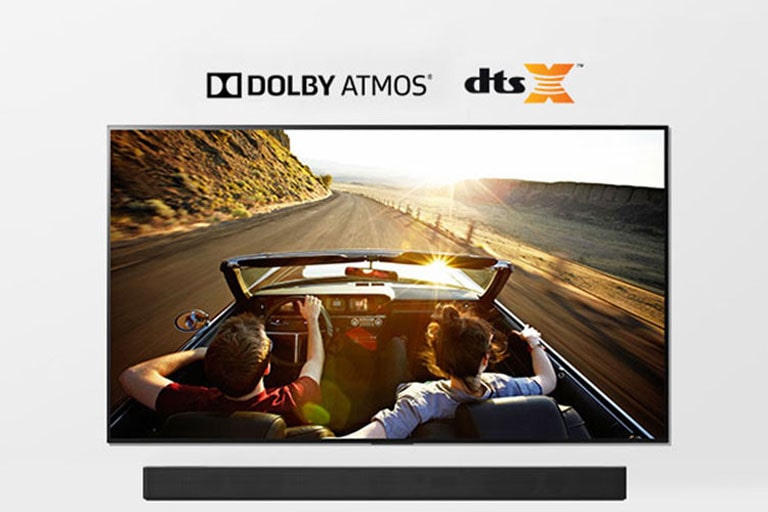 TV and Soundbar together in full view. TV shows a couple in an open roof car on the road driving into the sunset. 