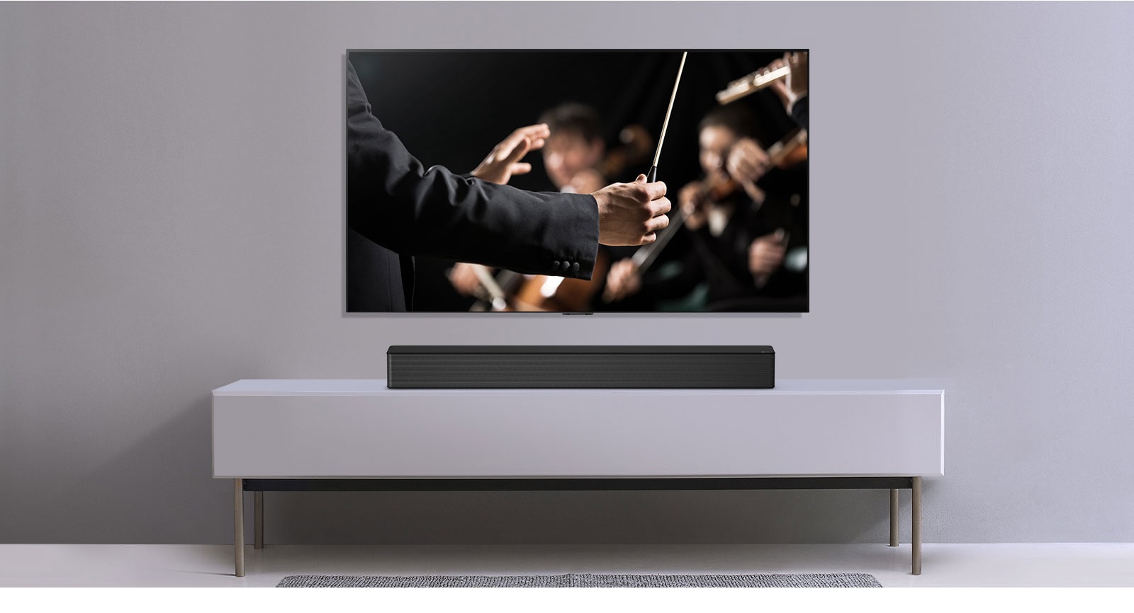 A TV is shown on a gray wall and LG Soundbar below it on a gray shelf. TV shows a conductor conducting an orchestra.