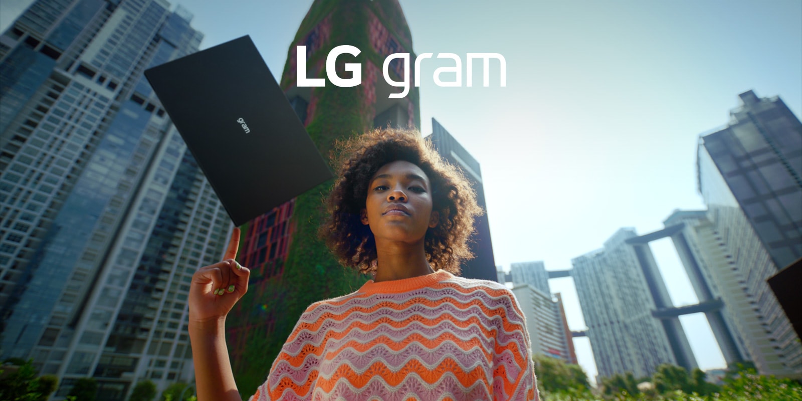 a woman with LG gram laptop on her finger looking down, buildings behind her