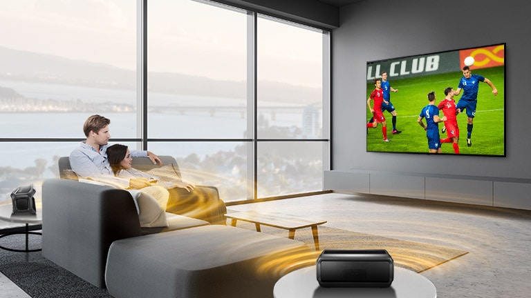 A man and women watching sports game on TV in the living room with Bluetooth rear speakers