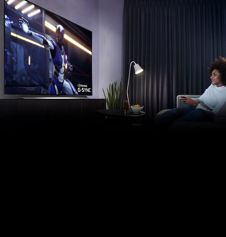 Woman sitting on a sofa, holding a joystick while playing a game on a TV screen