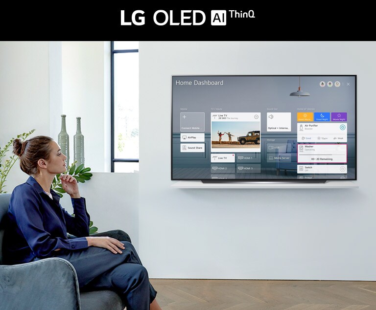 Woman sitting on a chair in the living room with the Home Dashboard on the TV screen