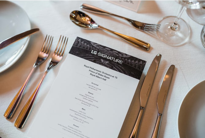 A menu with 'LG SIGNATURE' written at the top sits on a white table cloth with a fine dining table setting.