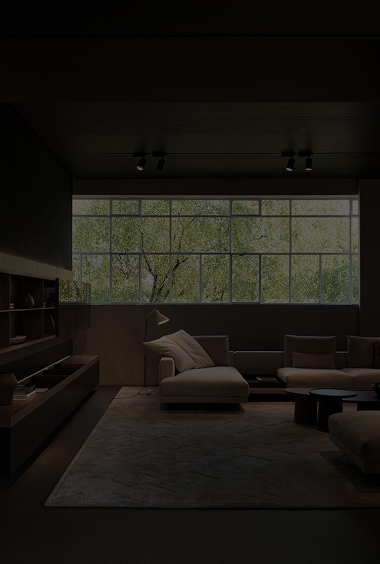 Couches and side tables are arranged in the living room with a long window across the whole wall.
