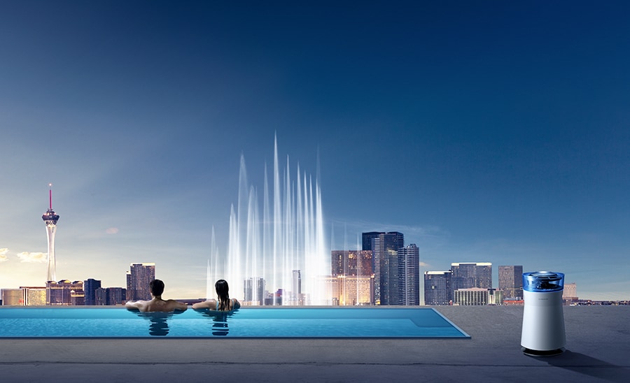 A couple are in a swimming pool observing the skyline of Las Vegas and the LG SIGNATURE's Air Purifier is placed next to the swimming pool.