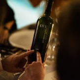 A bottle of LG SIGNATURE X LVE wine is held in people's hands.
