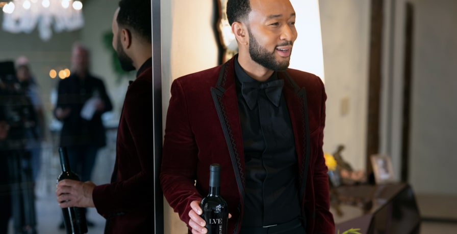 John Legend looks at the camera while holding the bottle of wine.