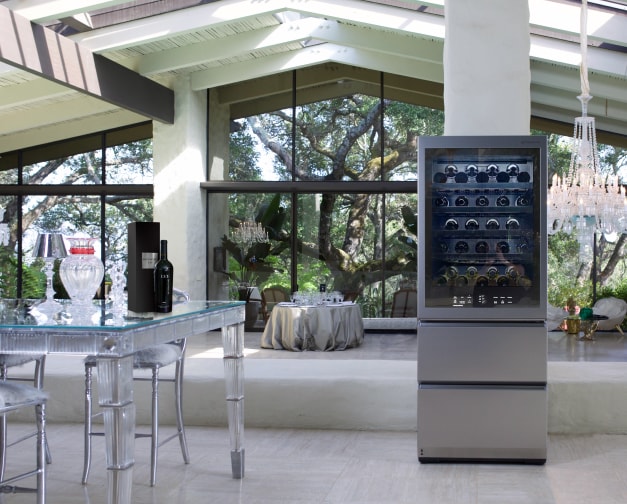 A wider shot of an interior featuring the wine cellar and a dining table with a wine bottle. The space is an empty, naturally-lit venue.