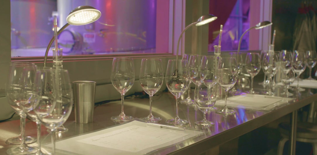 A bar table stacked with empty wine glasses, lamps, and a huge screen on the back wall.