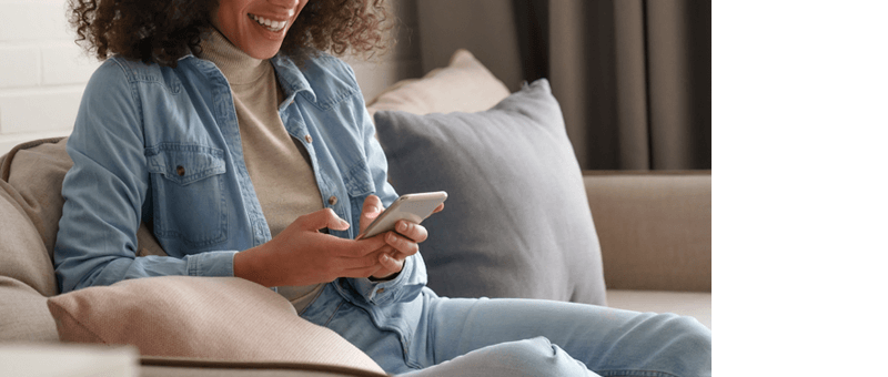 Woman Sitting on Couch Smiling While Registering for an LG Premium Care Plan From Her Phone.