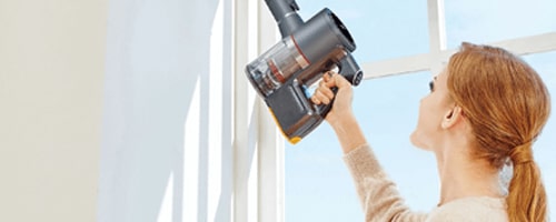 Woman Using the Crevice Tool Attachment (ABC73450101) on the LG CordZero Stick Vacuum to remove Dust from Hard-to-Reach Corner.