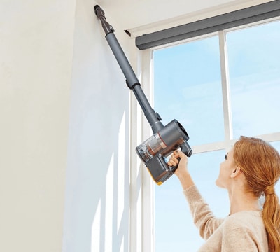 Woman Using the Crevice Tool Attachment (ABC73450101) on the LG CordZero Stick Vacuum to remove Dust from Hard-to-Reach Corner.