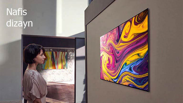 Ayol devorga osilgan televizorda namoyish qilinayotgan tasviriy sanʼat lavhasini tomosha qilmoqda.