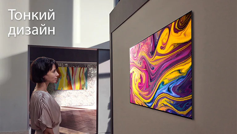 Женщина смотрит закрепленный на стене телевизор, на котором демонстрируется живопись.