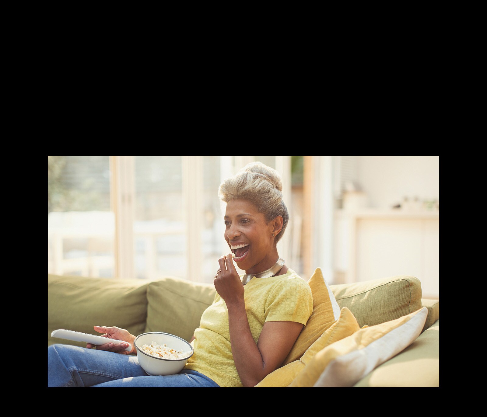 Женщина смотрит телевизор, держа в руках пульт дистанционного управления. Она ест попкорн.