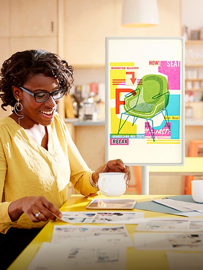 Hình ảnh thiết kế của chiếc ghế được hiển thị trên màn hình StanbyME đặt trong văn phòng, và một người phụ nữ đang họp và đồng thời nhìn vào tờ giấy.