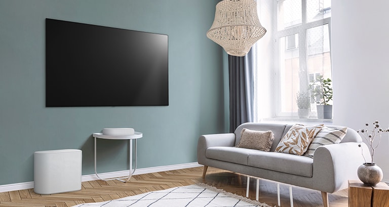 A soundbar is placed on a small tea table,  a subwoofer placed on the left side and TV is placed above a soundbar. The room is overall white.