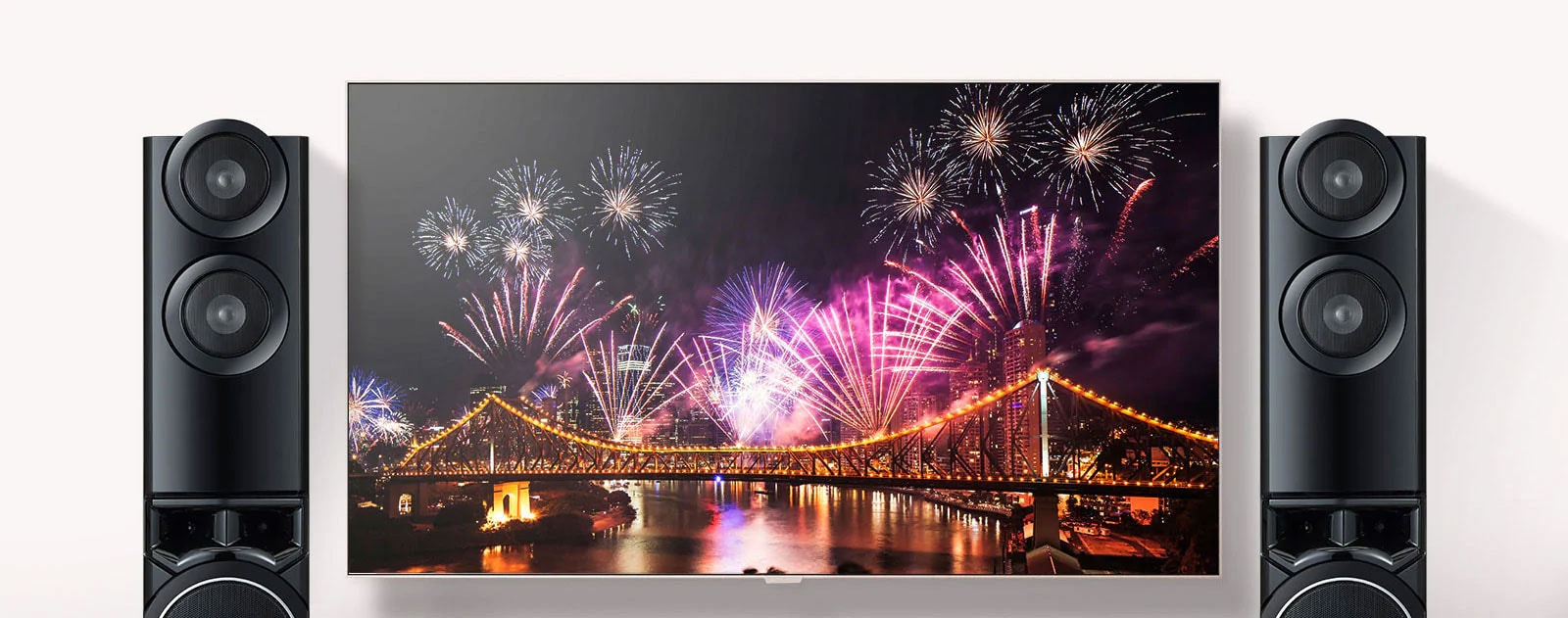 Between the two speakers, TV is on a wall. TV Shows fireworks spreading over the bridge.