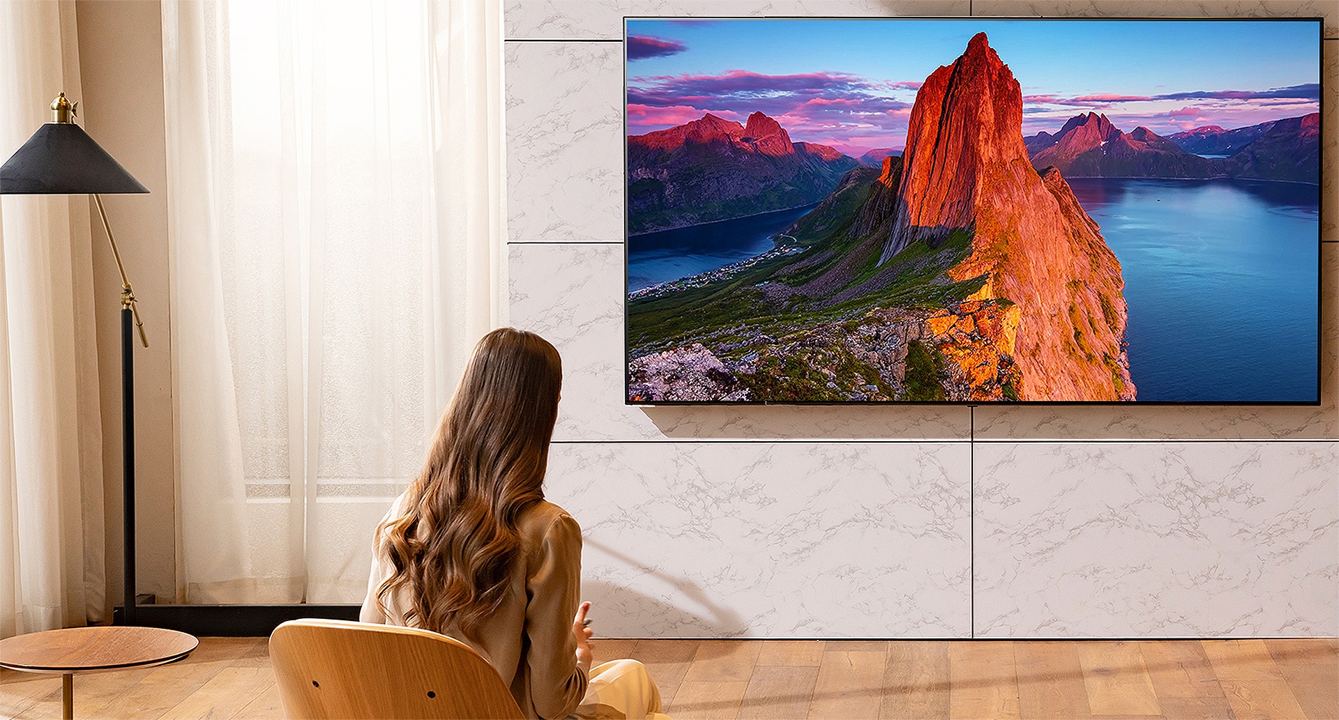 A woman is watching TV in the living room. Landscape scenery is on the screen.