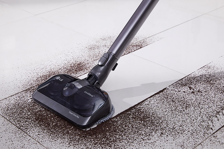 Der Power Drive Mop saugt den Schmutz auf und man sieht eine gerade Linie von weißem, sauberem Boden inmitten des Chaos, da er alles mühelos aufsaugt.