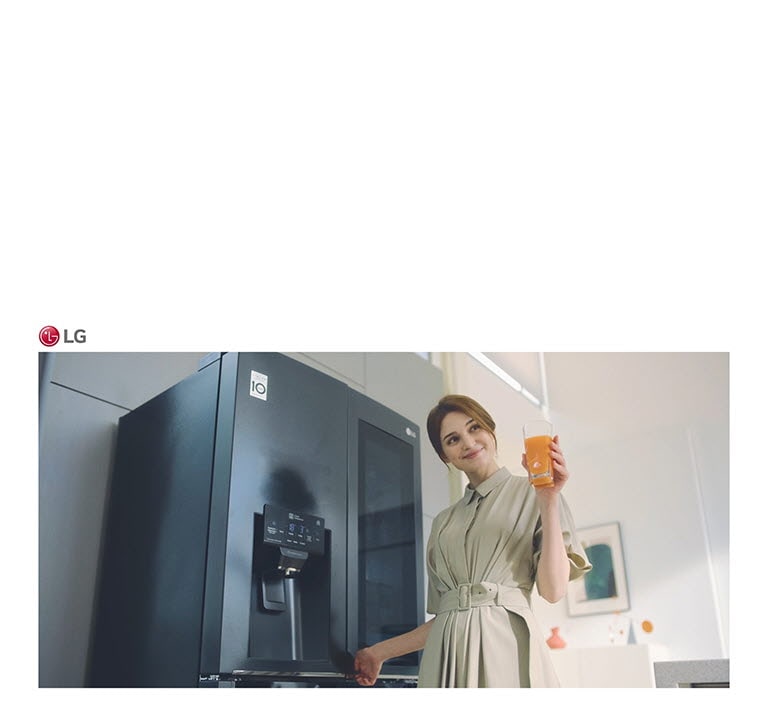 Eine Frau steht vor dem Kühlschrank, hält ein Glas Saft in der Hand und lächelt, als sie die Tür schließt.