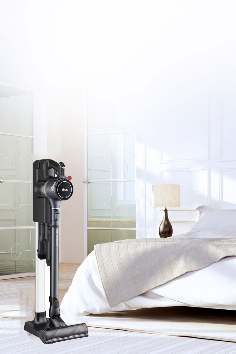 Der CordZero A9 Kompressor-Staubsauger steht in der Ladestation in einem Schlafzimmer neben einem Bett.