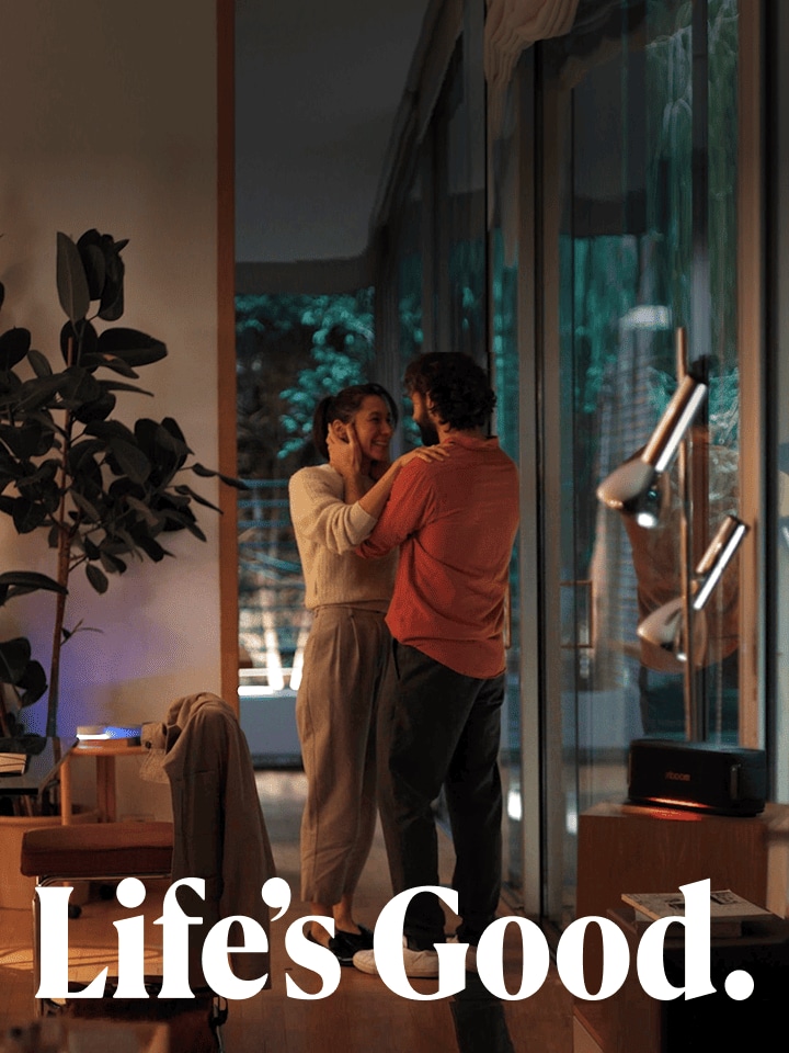 Un hombre y una mujer se miran y sonríen. La habitación se ve cálida y tranquila. La imagen tiene un texto en blanco que dice "Life's good".