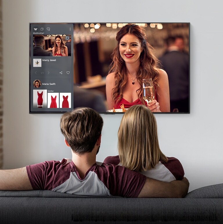 Una pareja sentada en un sofá viendo un televisor que muestra a una mujer y la información del producto de un vestido rojo que lleva la mujer.