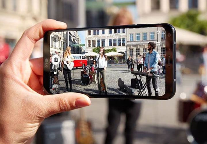 A person holding new lg q6 to take a photo of street performers.