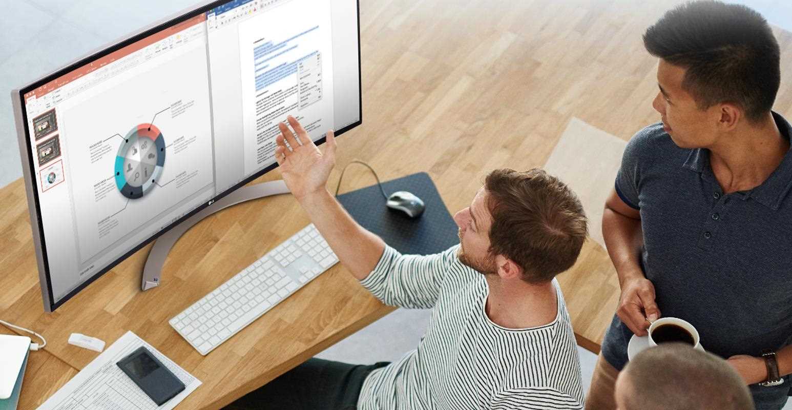 Colleagues collaborate at an ergonomic workstation with an ultrawide monitor.