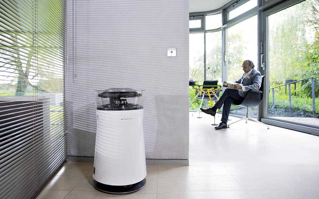 LG SIGNATURE air purifier in a hallway while a man works in his office with a view of the garden