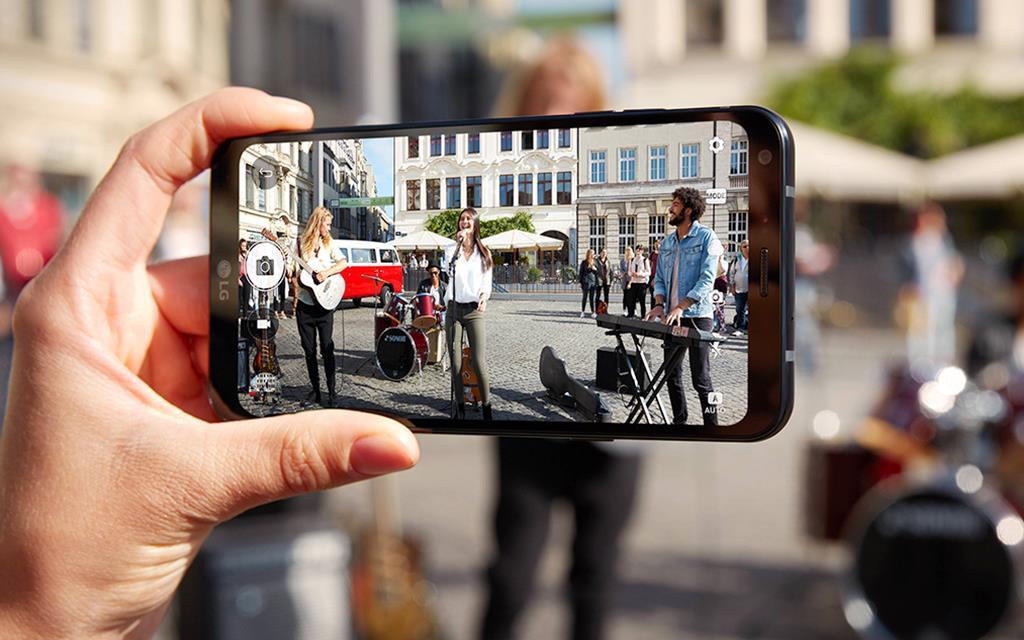A person holding new lg q6 to take a photo of street performers.