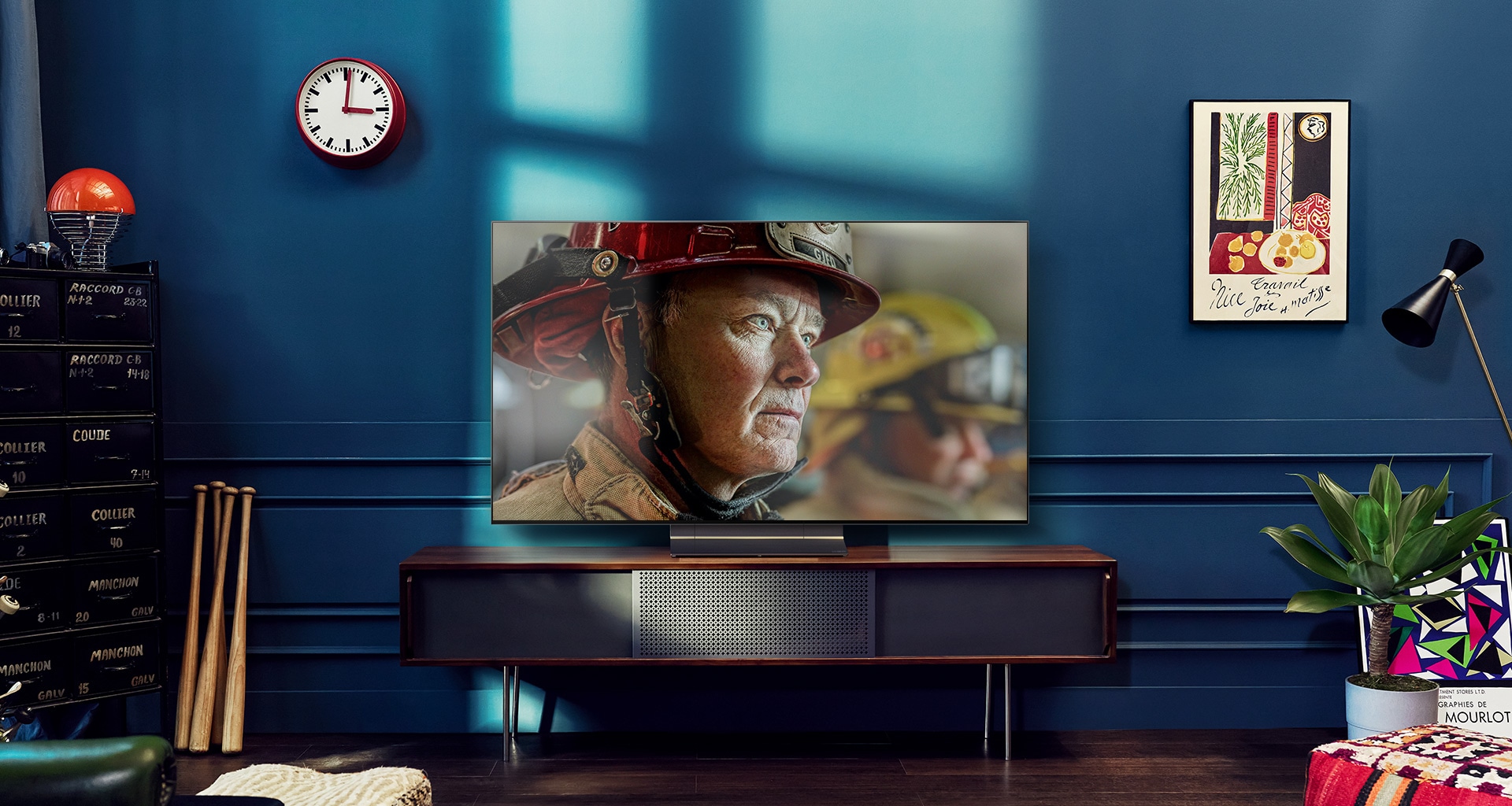 A wall-mounted LG OLED TV is in a white and bright room with natural decorations. As the screen moves, the scene changes from day to night. with Dolby Vision IQ logo
