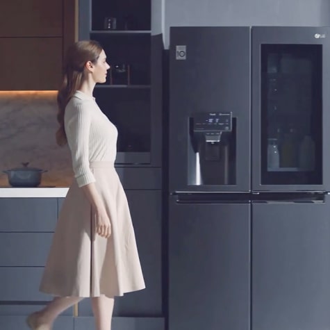 A woman walks towards the LG Dios refrigerator.