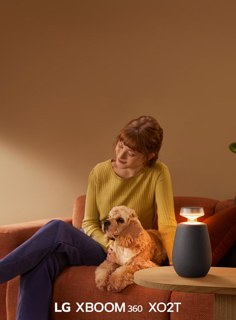 Una mujer sentada en el sofá con su perro y escuchando música con LG XBOOM 360 XO2T.