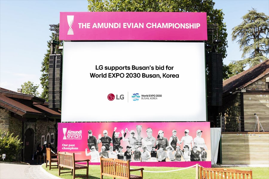 A large pink billboard in a park setting promoting the Amundi Evian Championship and LG's support for Busan's World EXPO 2030 bid.