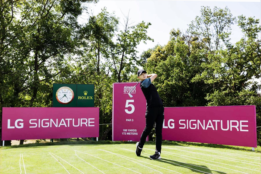 A golfer dressed in black attire swings at a tee box labeled '5', with signs advertising LG SIGNATURE in the backdrop.