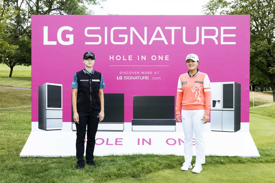 A pink LG Signature ad on a golf course, featuring product imagesVwith two people standing in the foreground against a verdant landscape.