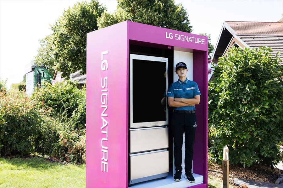 An LG Signature booth in purple with a black screen, accompanied by a woman standing next to it.